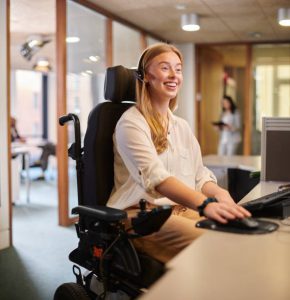 woman in a power wheelchair working at a desk in a office